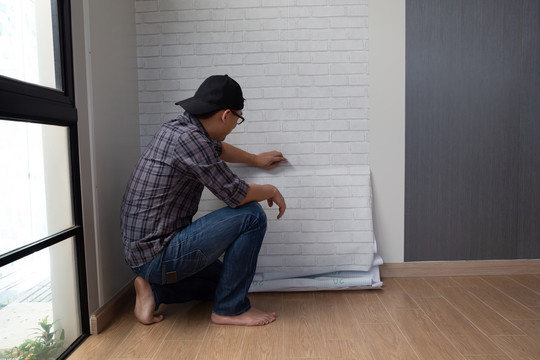 年轻的亚洲男人在家里把墙纸粘在墙上。以自我diy理念改造室内空间