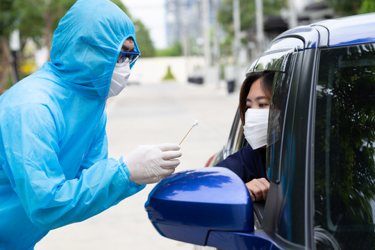穿着PPE防护服的护士或穿着全套防护装备的医务人员从车内女司机处采集样本。冠状病毒2019冠状病毒疾