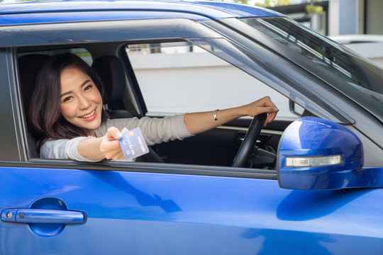 快乐的年轻亚洲女性，持有支付卡或信用卡，曾在加油站支付汽油、柴油和其他燃料的费用，司机持车队卡为汽车