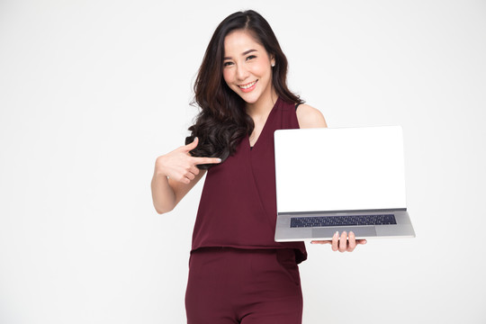 年轻的亚洲女商人在白色背景上展示笔记本电脑，并将手指指向笔记本电脑的白色屏幕，屏幕上有用于在线展示应