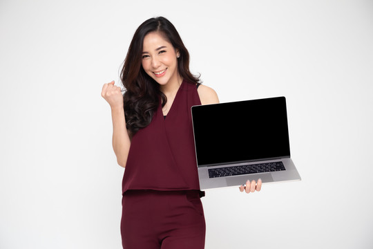 一位兴奋的亚洲女性手持笔记本电脑，在白色背景下庆祝成功，带着幸福的表情举起手臂，这是一幅女性模特的画