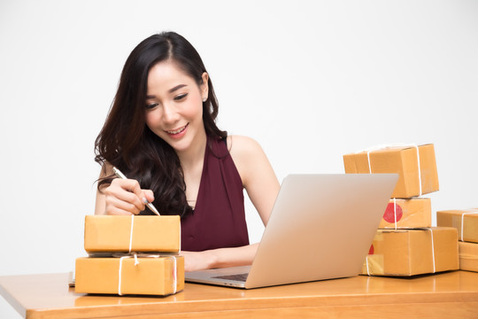 亚洲女性将包裹放在桌子上，白色背景，女性通过网上订购、送货和网上购物收到硬纸盒