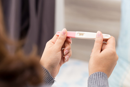 妇女手持排卵测试仪，正在试图怀孕时收集尿液放在测试条上，结果呈阳性