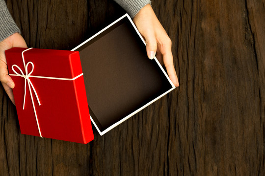 顶视图：女性手拿木制背景上的红色礼品盒，打开盒子，留出空间放置产品