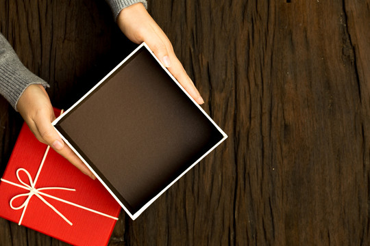 女性手拿木制背景上的红色礼品盒的俯视图，打开有空间放置产品的盒子