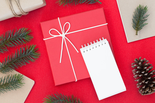 圣诞和新年快乐构图的俯视图、礼品盒、松果、红色背景上的冷杉枝以及文本的复制空间白皮书