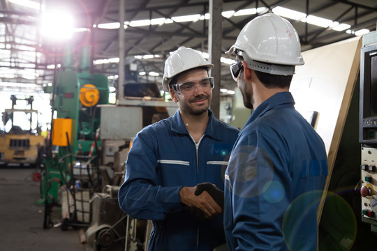 戴手套的重工业工人在金属制品工厂相互握手问候，团队合作和伙伴关系理念