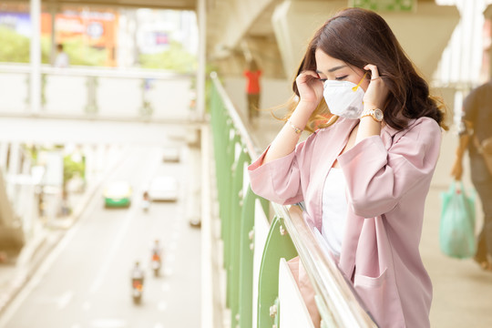 在空气污染严重的城市街道上，一位亚洲女商人戴着防护面罩。安全防护面罩户外环境意识概念