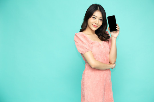 快乐的亚洲女人微笑着拿着手机，背景是浅绿色的