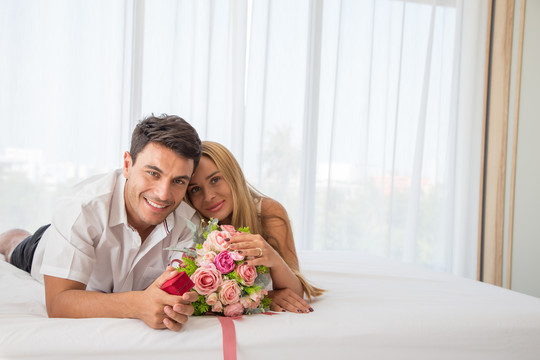 这对夫妇微笑着躺在床上，手里拿着鲜花，男人向他们求婚