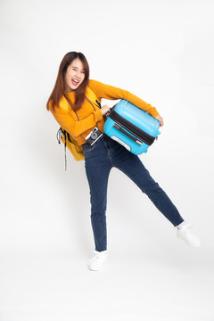 年轻的亚洲女旅行者，背着背包站着，提着白色背景的手提箱