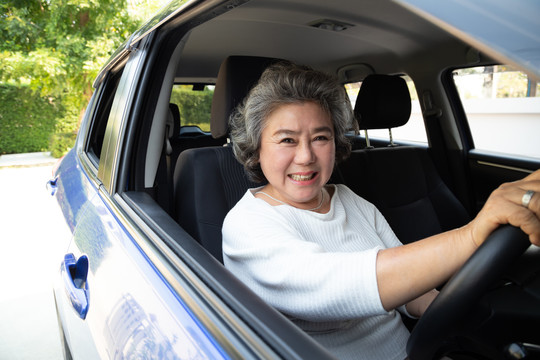 亚洲资深女性驾驶汽车，开心地微笑着，在驾车旅行的过程中，人们享受着欢笑的交通和免下车的概念