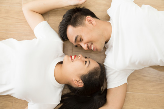 亚洲夫妇相互对视，躺在家里的地板上，这是真爱和婚前摄影的概念