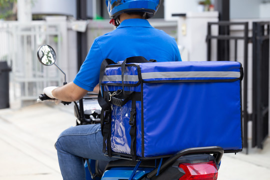 身穿蓝色制服的送货员骑着摩托车和送货箱。提供食物或包裹快递服务的摩托车