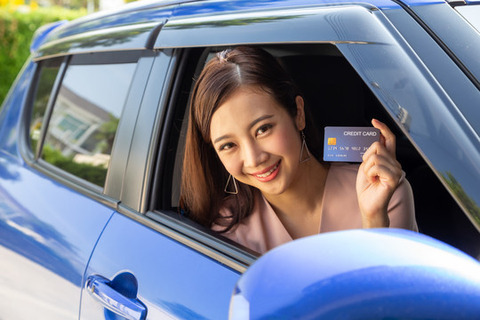 坐在车里，手里拿着支付卡或信用卡的快乐年轻亚洲女人