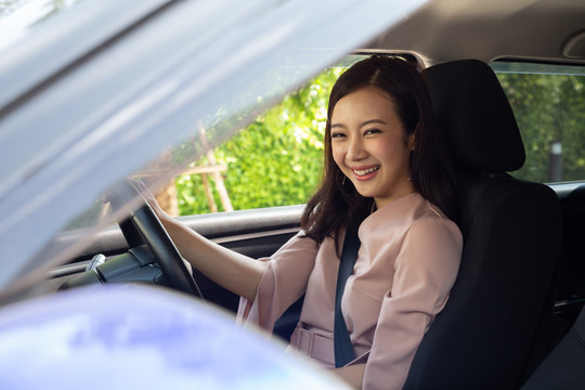 在工作日开车去办公室的路上，快乐的亚洲女性开着车，带着快乐的积极表情微笑着