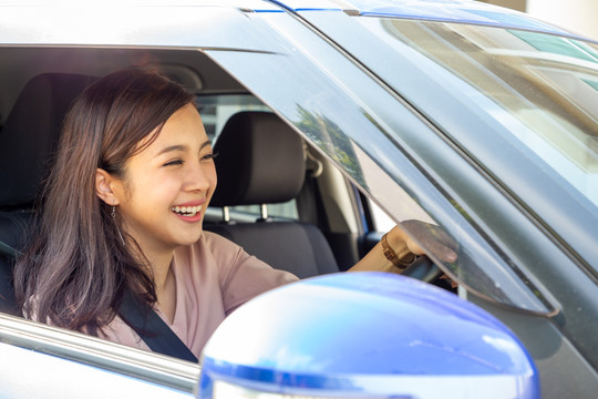 年轻的亚洲女性开车并系好安全带，在开车去旅行的过程中带着快乐的积极表情，轻松的微笑，快乐的女性在公路