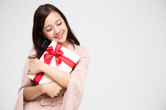 快乐美丽的亚洲女性微笑着拥抱白色背景上的礼品盒。少女坠入爱河，接受情人的礼物。新年、圣诞节和情人节概