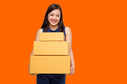 快乐的亚洲女人拿着橙色背景的包裹盒，快递和运输服务理念
