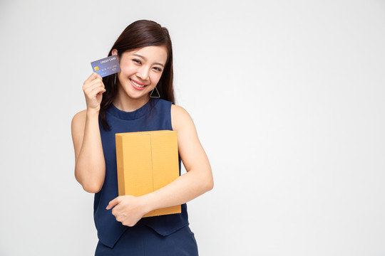 快乐亚洲女子手握包裹盒和信用卡，送货上门服务和网上购物理念