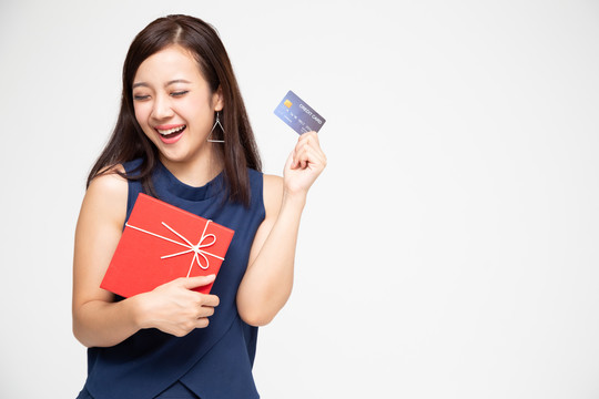 快乐的亚洲美女手上拿着红色礼品盒和信用卡，背景为白色