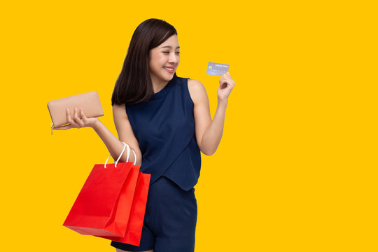 亚洲女性使用信用卡，喜欢在黄色背景上购物