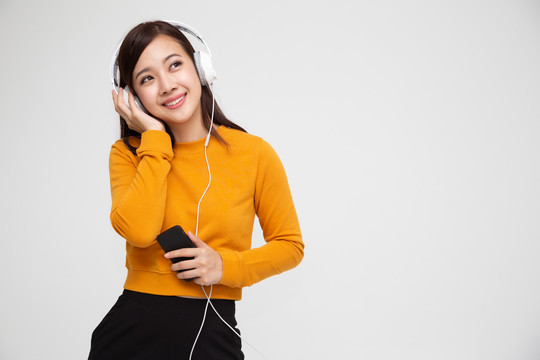 年轻的亚洲美女戴着耳机在白色背景上隔离的智能手机上播放歌曲应用程序