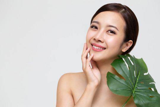 快乐美丽的年轻亚洲女性，拥有干净清新的皮肤和绿叶，女孩美容面部护理，面部护理和美容spa概念