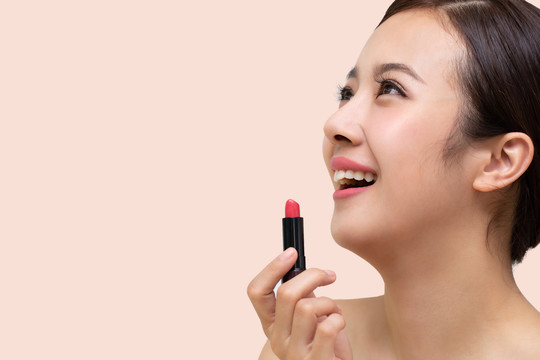 美丽的亚洲女人在粉色背景下夹着唇膏
