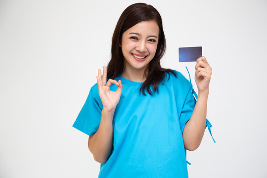 年轻的亚洲美女患者在白色背景上展示个人意外保险护理卡和ok标志，PA和健康索赔服务理念