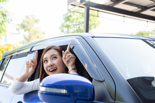 快乐的亚洲女人坐在车里，指着车顶上的空白复印区
