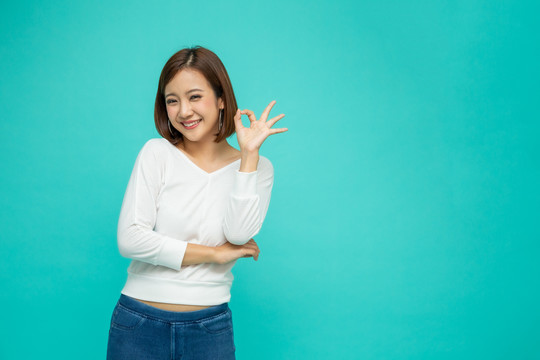 快乐的亚洲年轻女性的肖像，手势或举手ok，看着隔离在绿色背景上的相机，女性感觉积极和享受概念