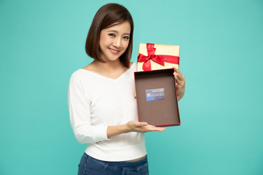 亚洲女性手持并展示金色礼品盒，打开盒子，将产品信用卡或礼品卡隔离在浅绿色背景上