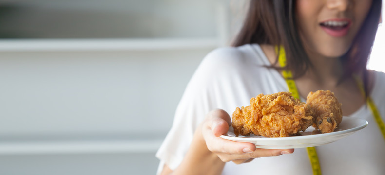 年轻的亚洲女性在盘子里拿着炸鸡、垃圾食品和减肥理念