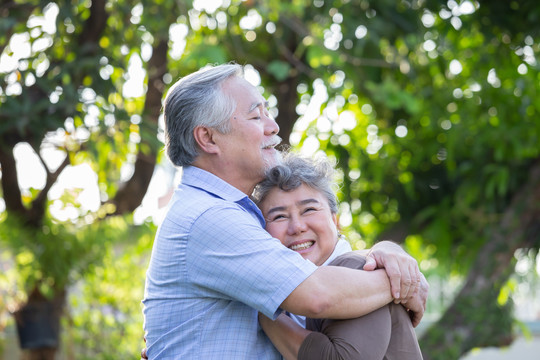 快乐成熟的情侣在花园里拥抱欢笑，亚洲老年人在户外拥抱，庆祝结婚周年