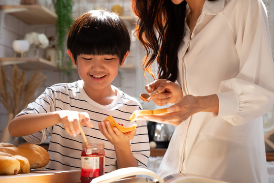 在家里的厨房里，母亲和儿子一起微笑着做饭，用面包和草莓酱做早餐。快乐生活活动理念
