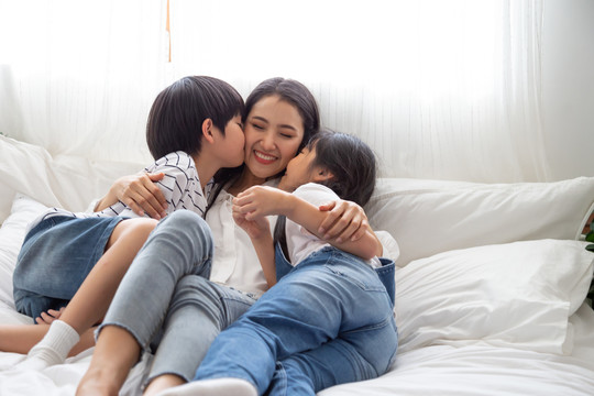 亚洲家庭的幸福与母亲、儿子和女儿在卧室的白色床上拥抱和亲吻母亲，感受幸福和家庭关系概念