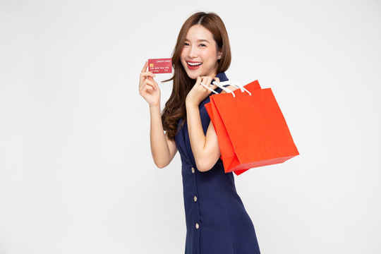 在白色背景下，一名手持信用卡和红色购物袋的亚洲年轻女子被隔离
