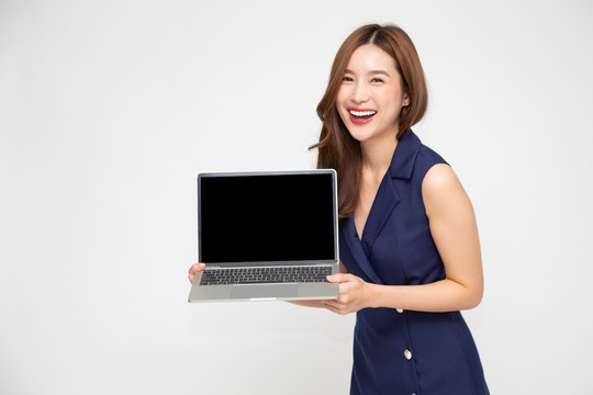 快乐的亚洲女商人在白色背景上展示空白笔记本电脑屏幕，看着相机