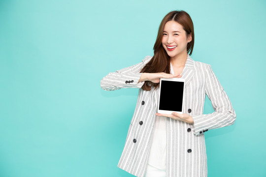 快乐的亚洲女人微笑着，手持平板电脑，背景为浅绿色