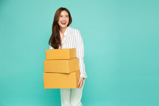快乐亚洲女子手持包裹包裹盒，以浅绿色为背景，提供快递和货运服务理念