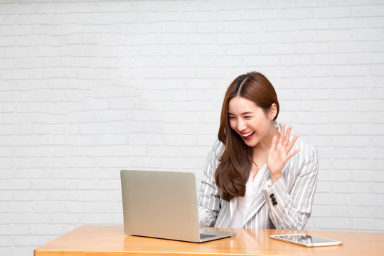 年轻的亚洲女性在家工作时看着笔记本电脑微笑，视频会议电话或在线培训理念