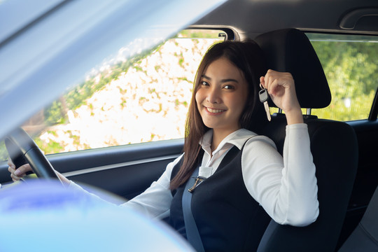亚洲女司机微笑着展示新车钥匙，坐在车内