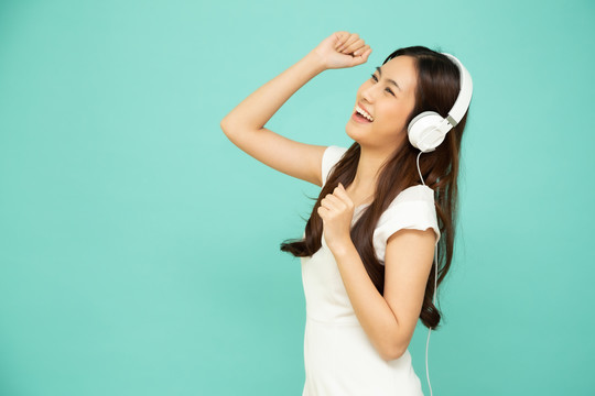 在绿色背景上隔离的智能手机上，年轻的亚洲美女戴着耳机在播放列表歌曲应用程序中跳舞和听音乐