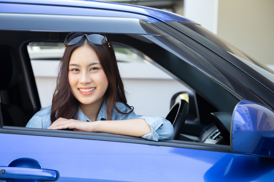 亚洲女性开车，带着快乐的笑容，在驾车旅行的过程中，人们享受着欢笑的交通和免下车的概念
