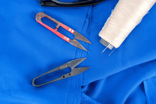蓝色布料背景上的针线剪刀等裁剪
