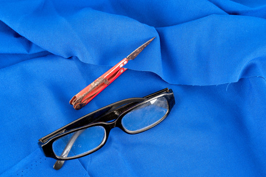 蓝色布料背景上的剪刀和眼镜