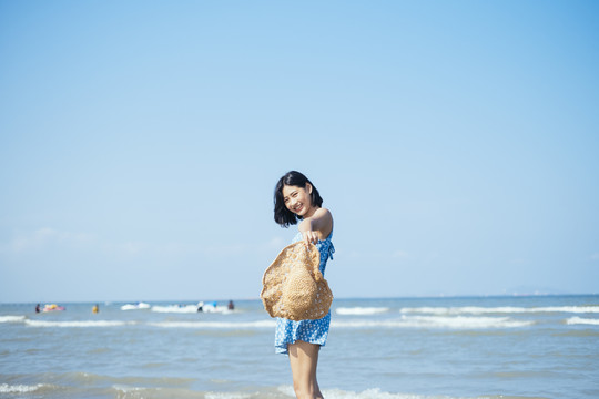 站在海边的海滩上，可爱的女孩微笑着给了相机一顶帽子。