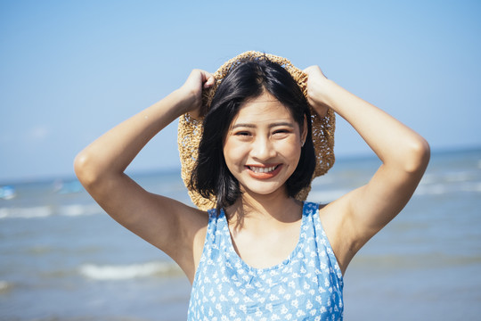 在刮风的日子里，快乐可爱的黑发女孩在海边把帽子戴在脑后。