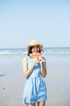 夏天，可爱的黑发女孩在海滩上拿着一块西瓜。